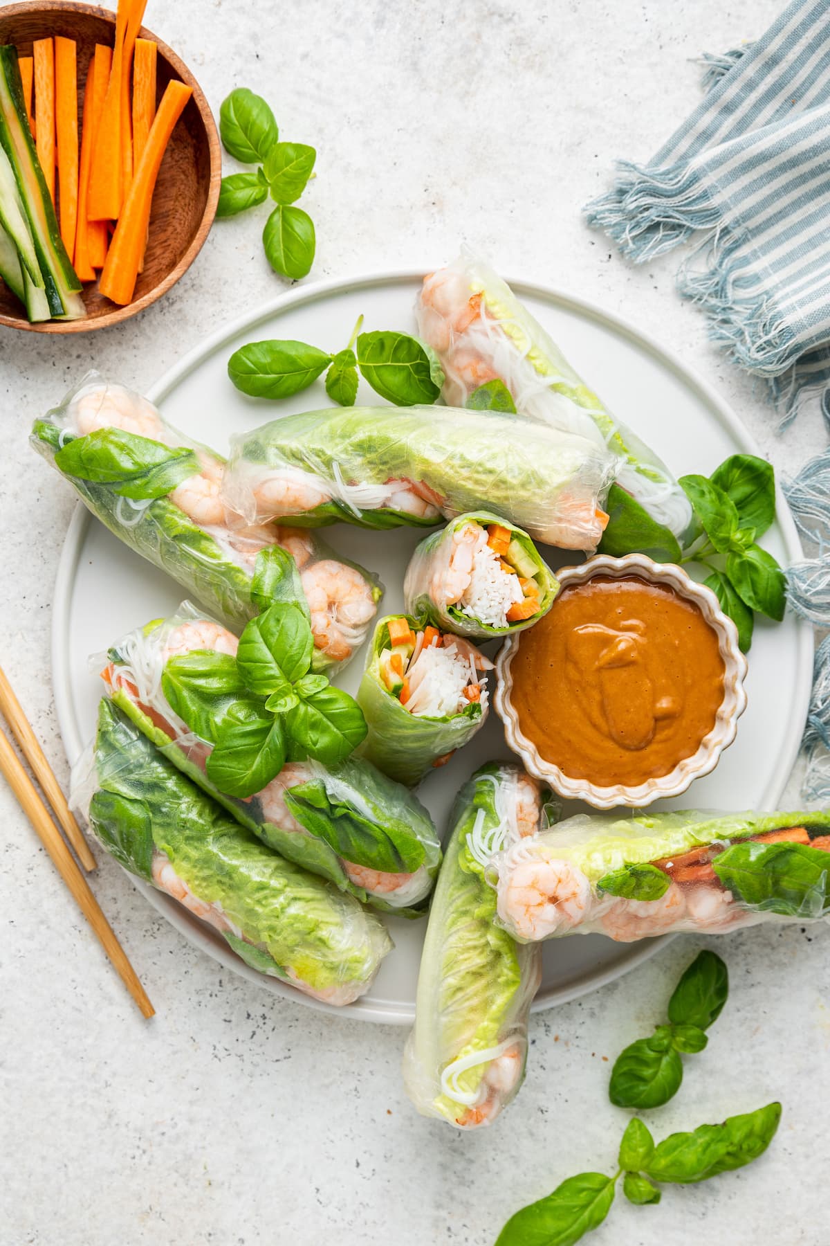 A large white plate with chopsticks containing multiple shrimp spring rolls, some cut in half, and a peanut sauce in a small white bowl.