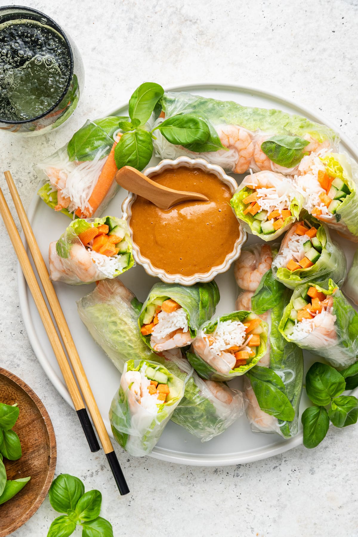 A large white plate with chopsticks containing multiple shrimp spring rolls, some cut in half, and a peanut sauce in a small white bowl.