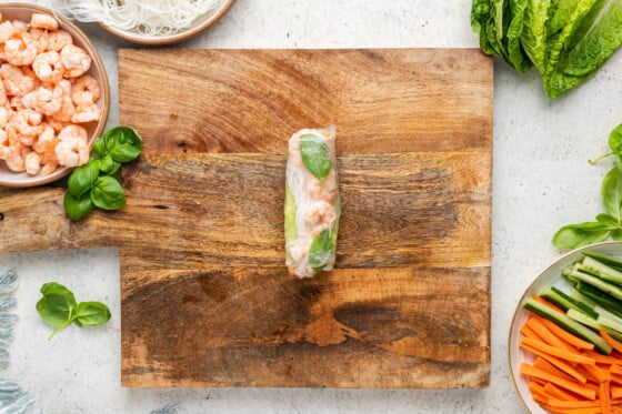 A shrimp spring roll in the center of a wooden cutting board.