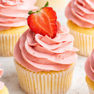 A cupcake with a pink strawberry buttercream frosting and a halved strawberry on top.