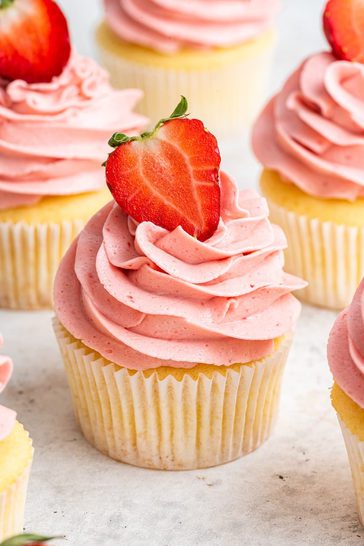 A cupcake with a pink strawberry buttercream frosting and a halved strawberry on top.