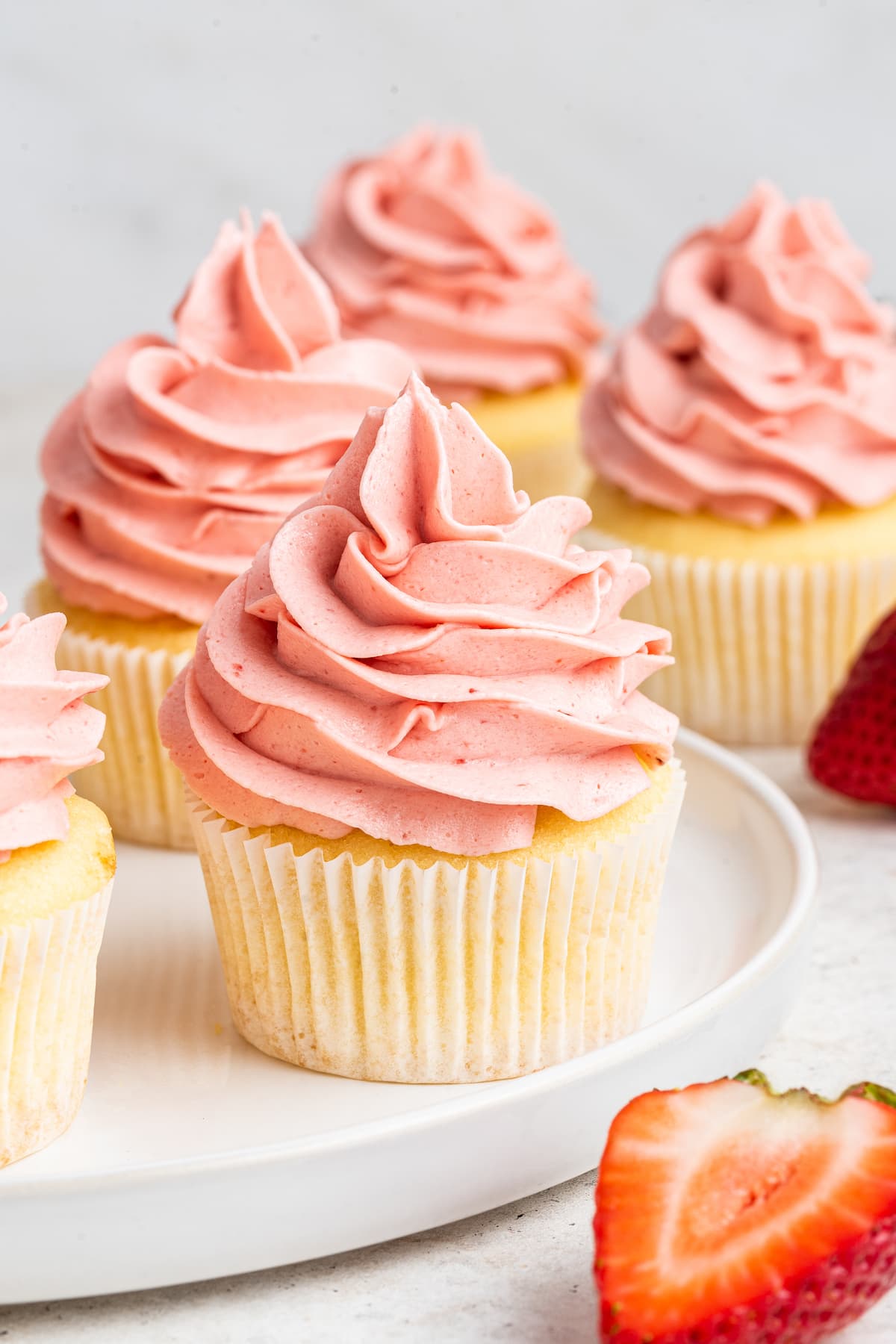 Multiple vanilla cupcakes on a white plate topped with a bright pink frosting.