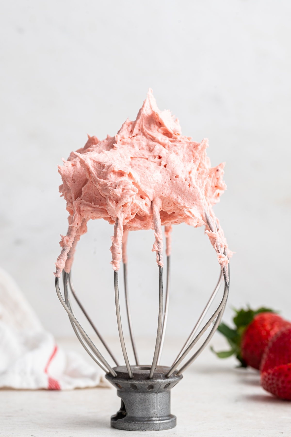 A kitchenmaid whisk standing upright with a lot of strawberry buttercream frosting on top.