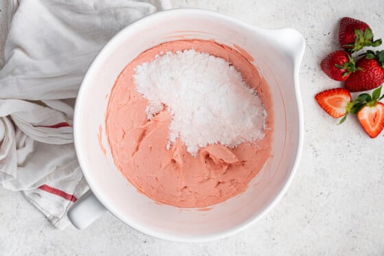 A pink strawberry buttercream frosting in a white bowl, with powdered sugar on top.