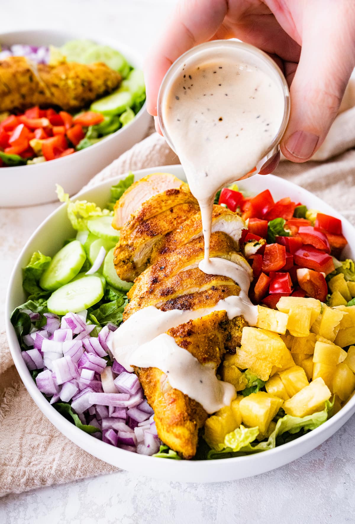 A woman's hand pouring dressing into a bowl of Thai curry chicken salad.