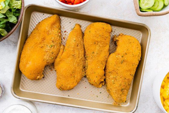 Four seasoned chicken breasts on a baking tray.