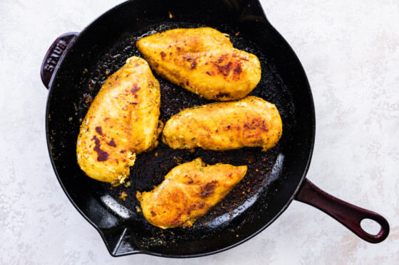 Four cooked chicken breasts in a cast iron skillet.