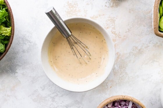 A white bowl with a metal whisk and a creamy dijon mustard dressing.