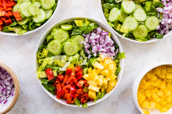 A large white bowl filled to the top with fresh salad ingredients, including cucumber, lettuce, red onion, red bell pepper, and pineapple.