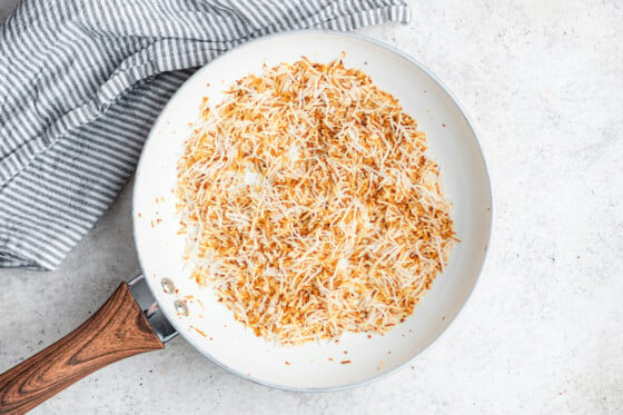 Toasted coconut shreds in a white skillet.