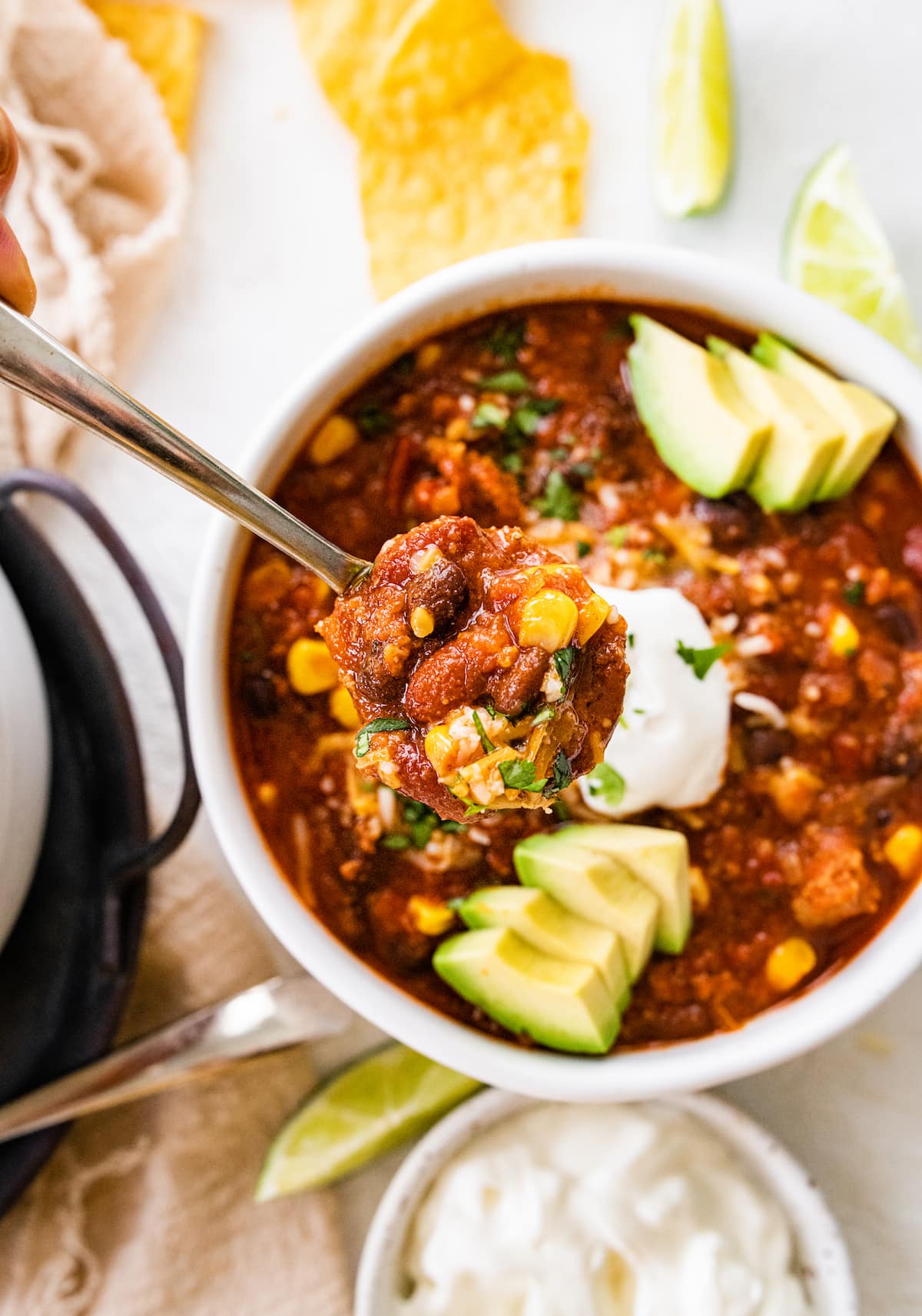 A spoonful of turkey chili being held over a white bowl of the chili.