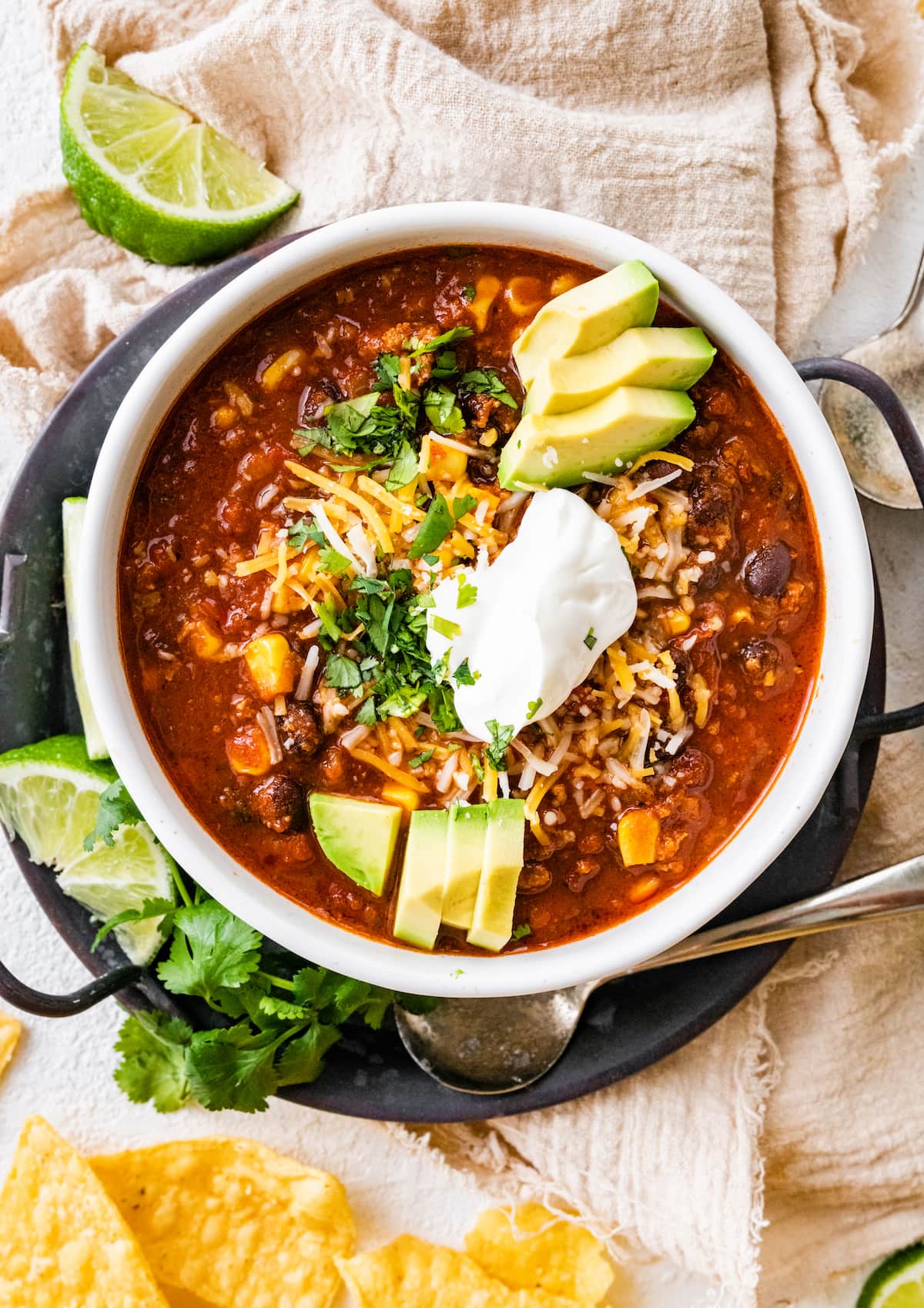 A white bowl full of turkey chili, topped sour cream, shredded cheese, avocado slices, and fresh cilantro.