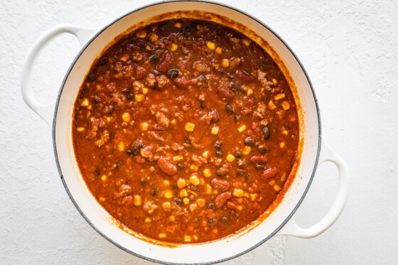 Turkey chili in a large, white dutch oven. Noticeable ingredients include corn, beans, and ground turkey.