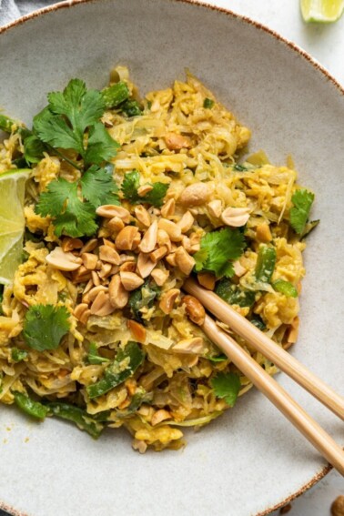 Healthy pad thai garnished with fresh cilantro and peanuts on a white plate with wooden chopsticks.