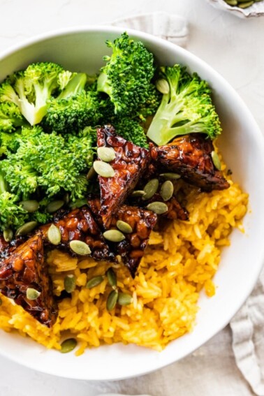 A white bowl with maple balsamic tempeh, broccoli, pumpkin seeds, and pumpkin rice.