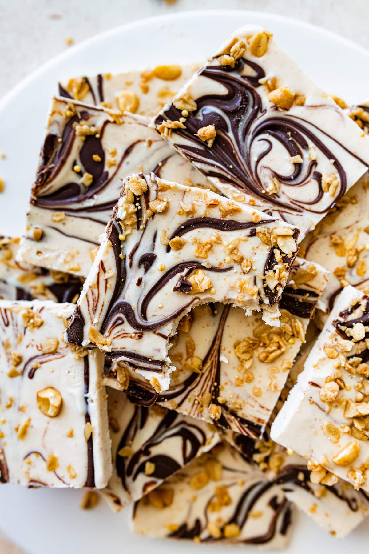 Frozen cottage cheese bark with dark chocolate and granola cut into squares and served on a white plate. The top piece has a bite taken out of it.