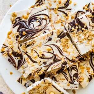 Frozen cottage cheese bark with dark chocolate and granola cut into squares and served on a white plate.