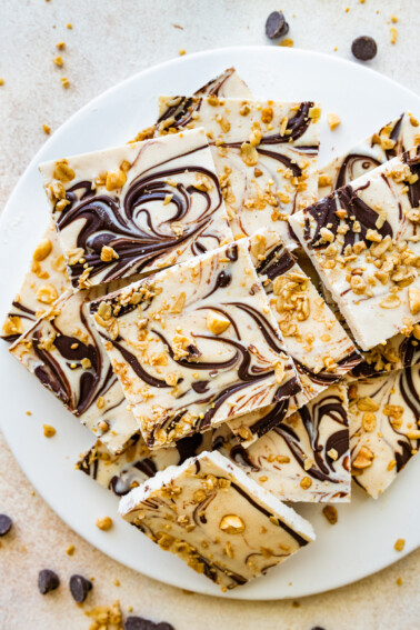 Frozen cottage cheese bark with dark chocolate and granola cut into squares and served on a white plate.