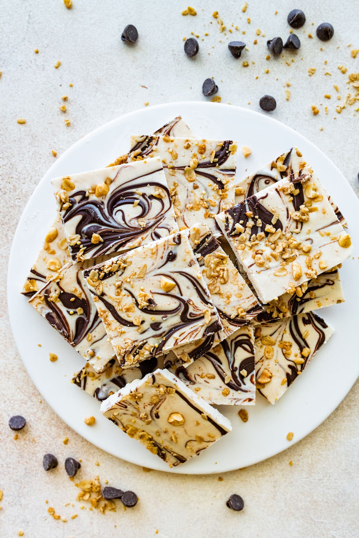 Frozen cottage cheese bark with dark chocolate and granola cut into squares and served on a white plate.