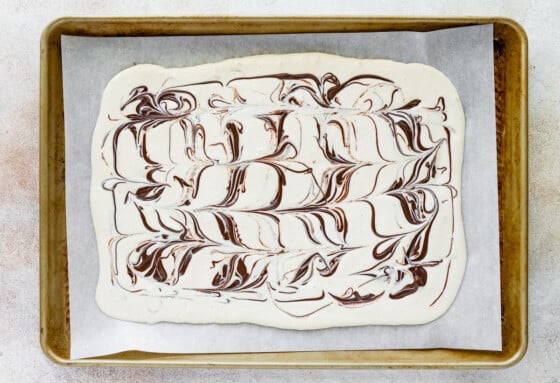 Cottage cheese bark mixture spread out onto a parchment lined baking tray with swirls of chocolate.