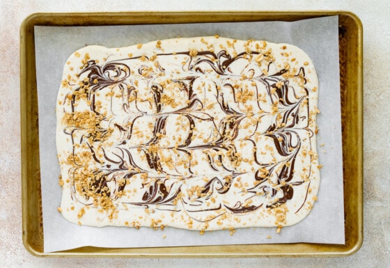 Cottage cheese bark mixture spread out onto a parchment lined baking tray with swirls of chocolate and topped granola.