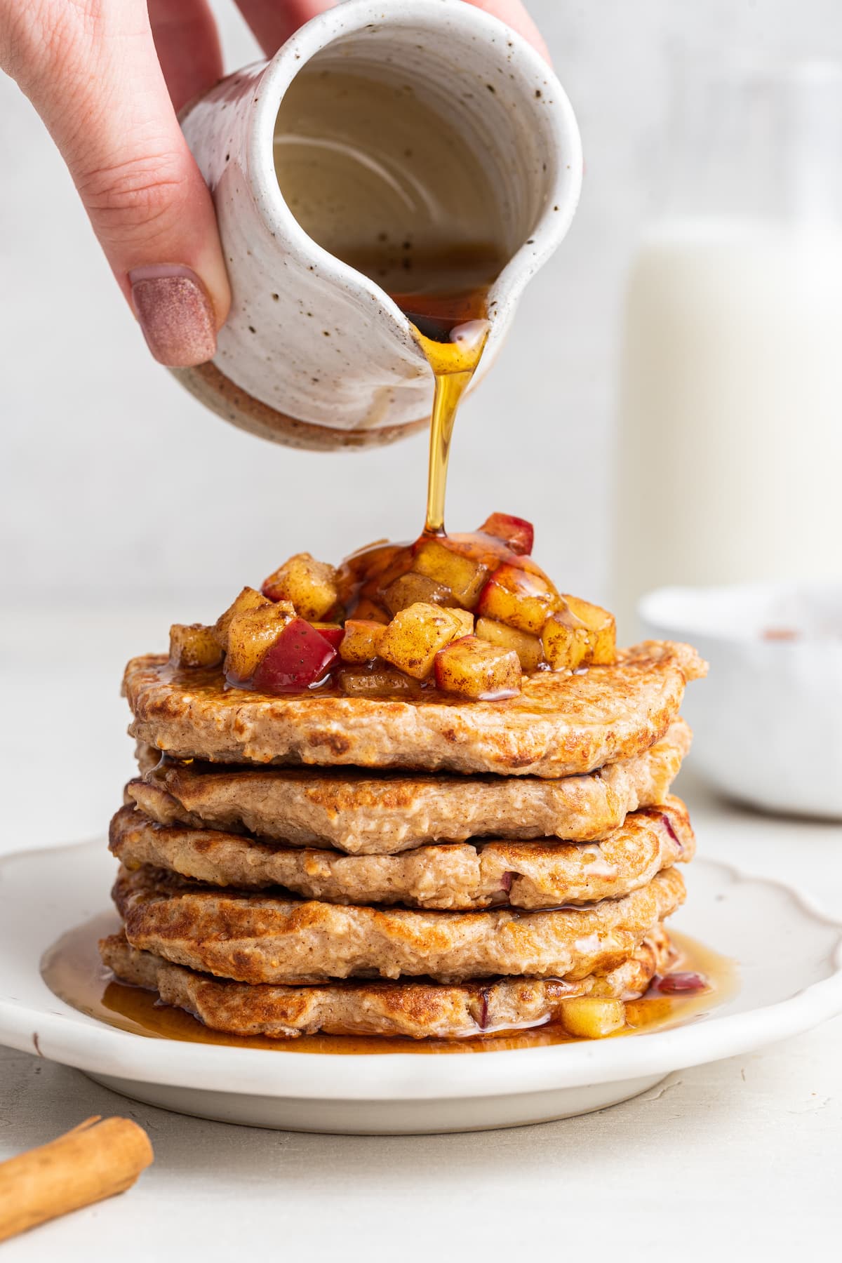 Woman's hand pouring maple syrup over a stack of apple pancakes.
