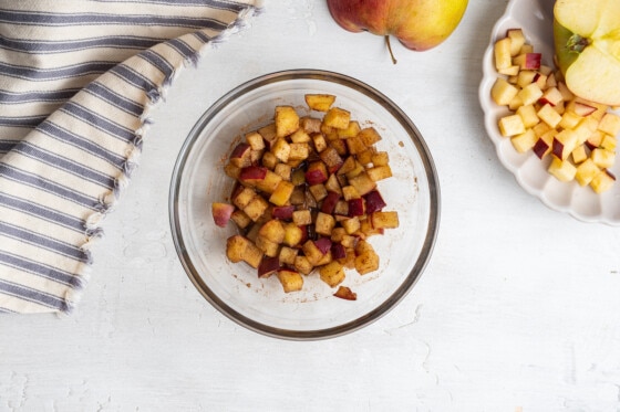 Diced apples mixed with cinnamon in a glass bowl.