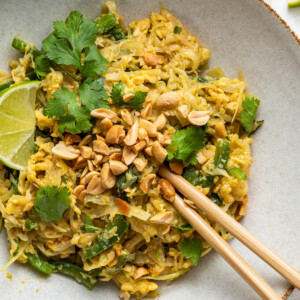 Healthy pad thai garnished with fresh cilantro and peanuts on a white plate with wooden chopsticks.