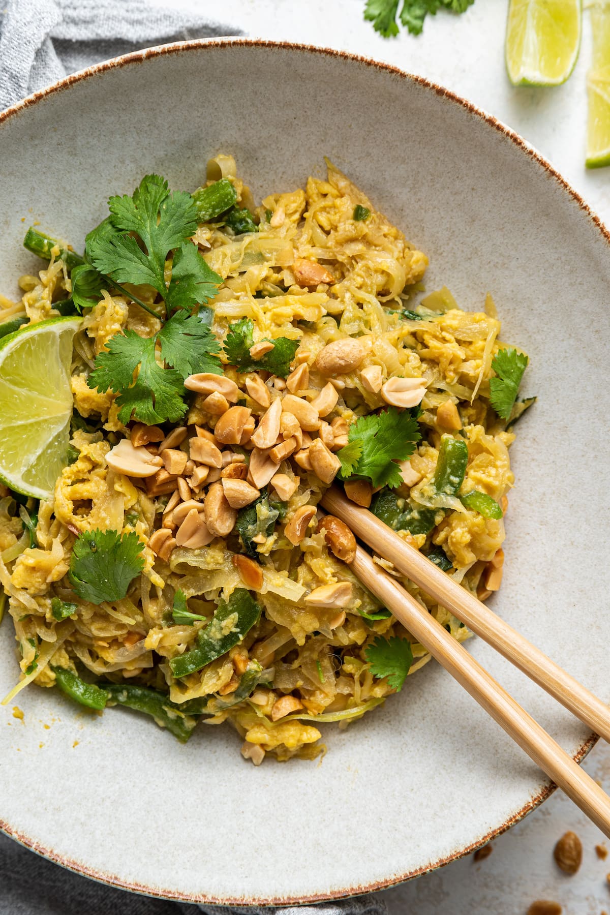 Healthy pad thai garnished with fresh cilantro and peanuts on a white plate with wooden chopsticks.