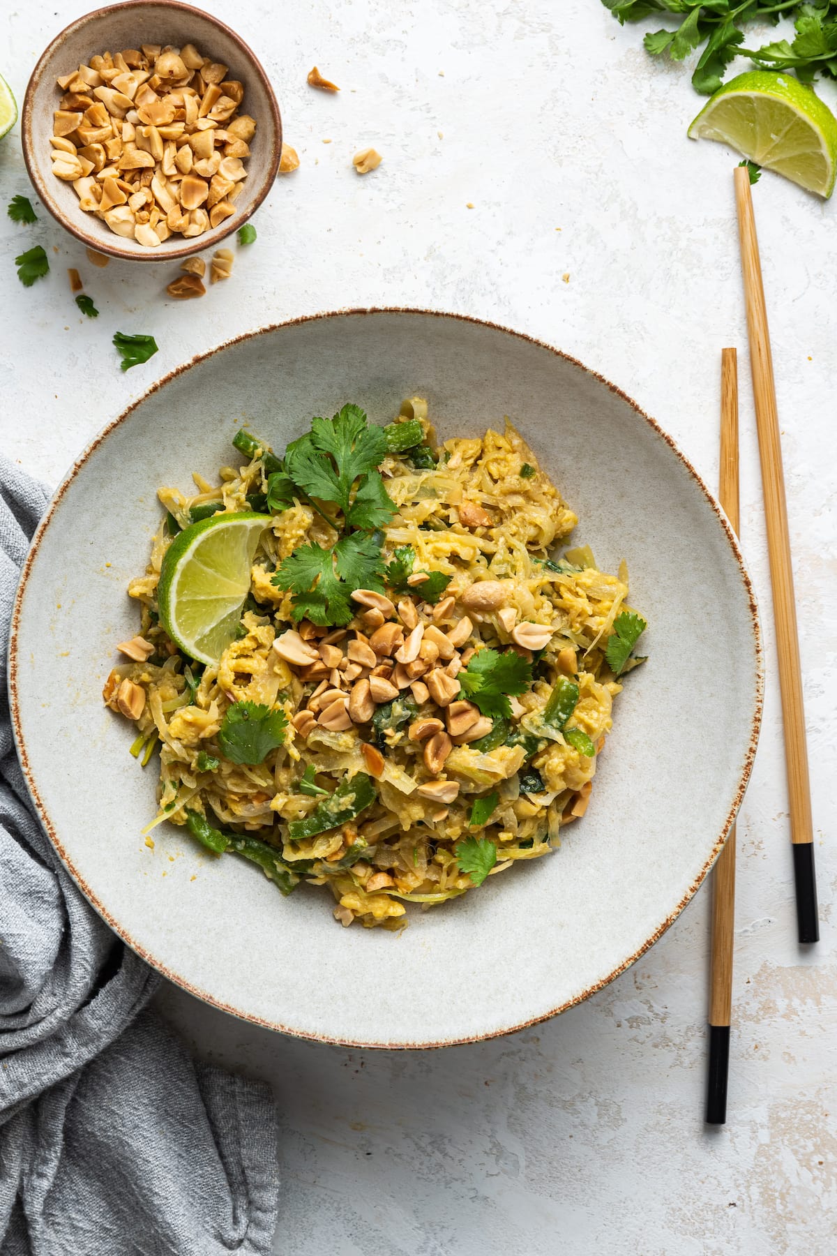 Healthy pad thai garnished with fresh cilantro and peanuts on a white plate with wooden chopsticks.