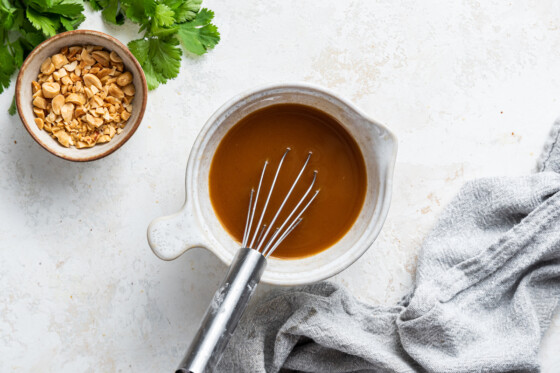 A small white bowl with a metal whisk and pad thai sauce.