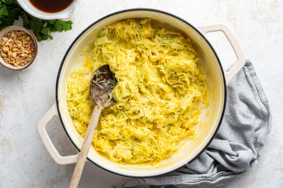 Shredded cabbage used in the healthy pad thai, in a large white pot with a wooden spoon.