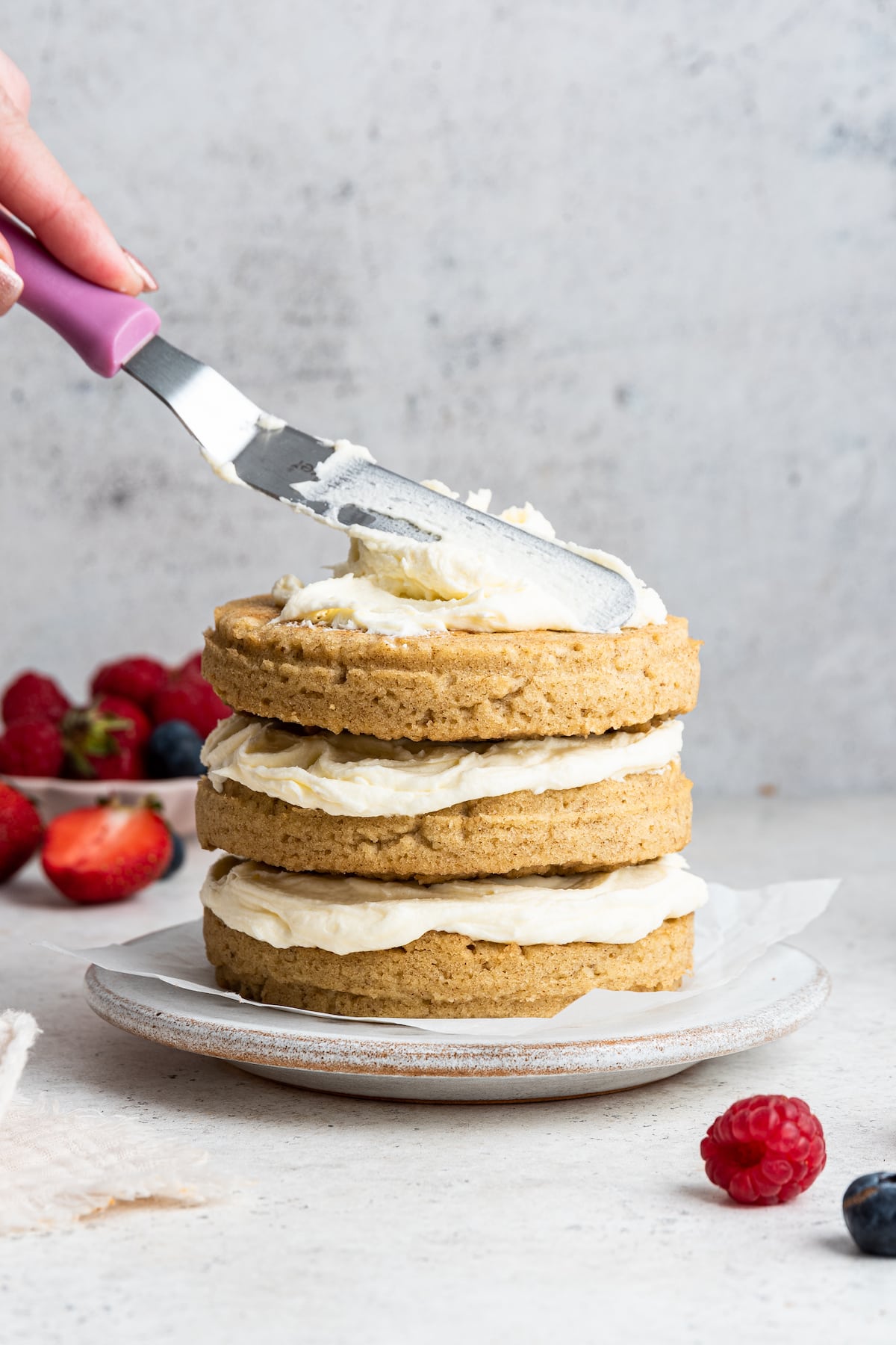 A woman's hand spreading the frosting onto the 3-layer smash cake.