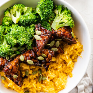 A white bowl with maple balsamic tempeh, broccoli, pumpkin seeds, and pumpkin rice.