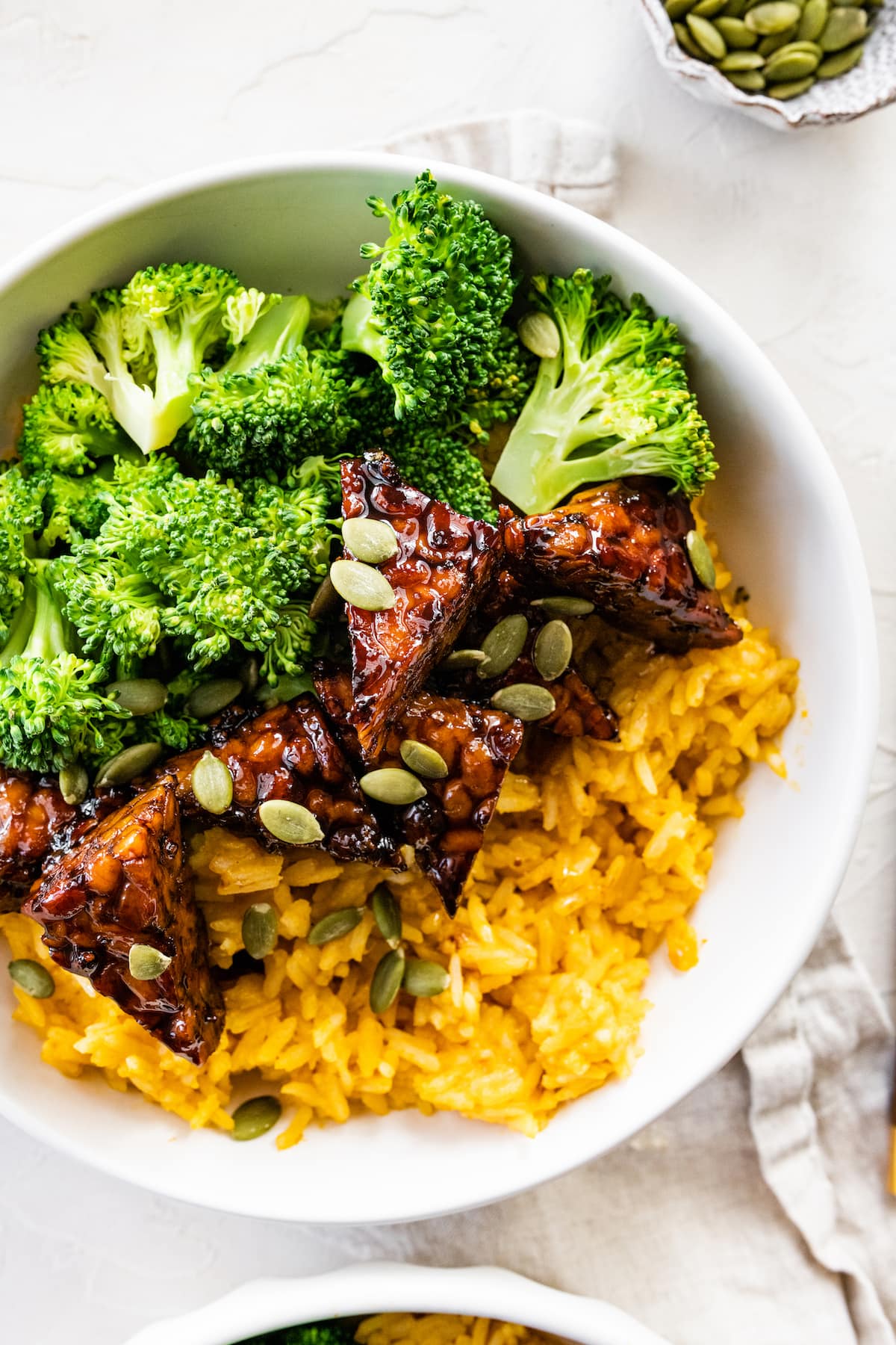 A white bowl with maple balsamic tempeh, broccoli, pumpkin seeds, and pumpkin rice.