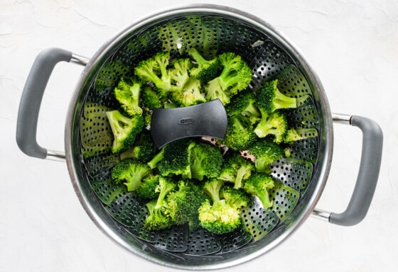 Broccoli florets in a metal colander.