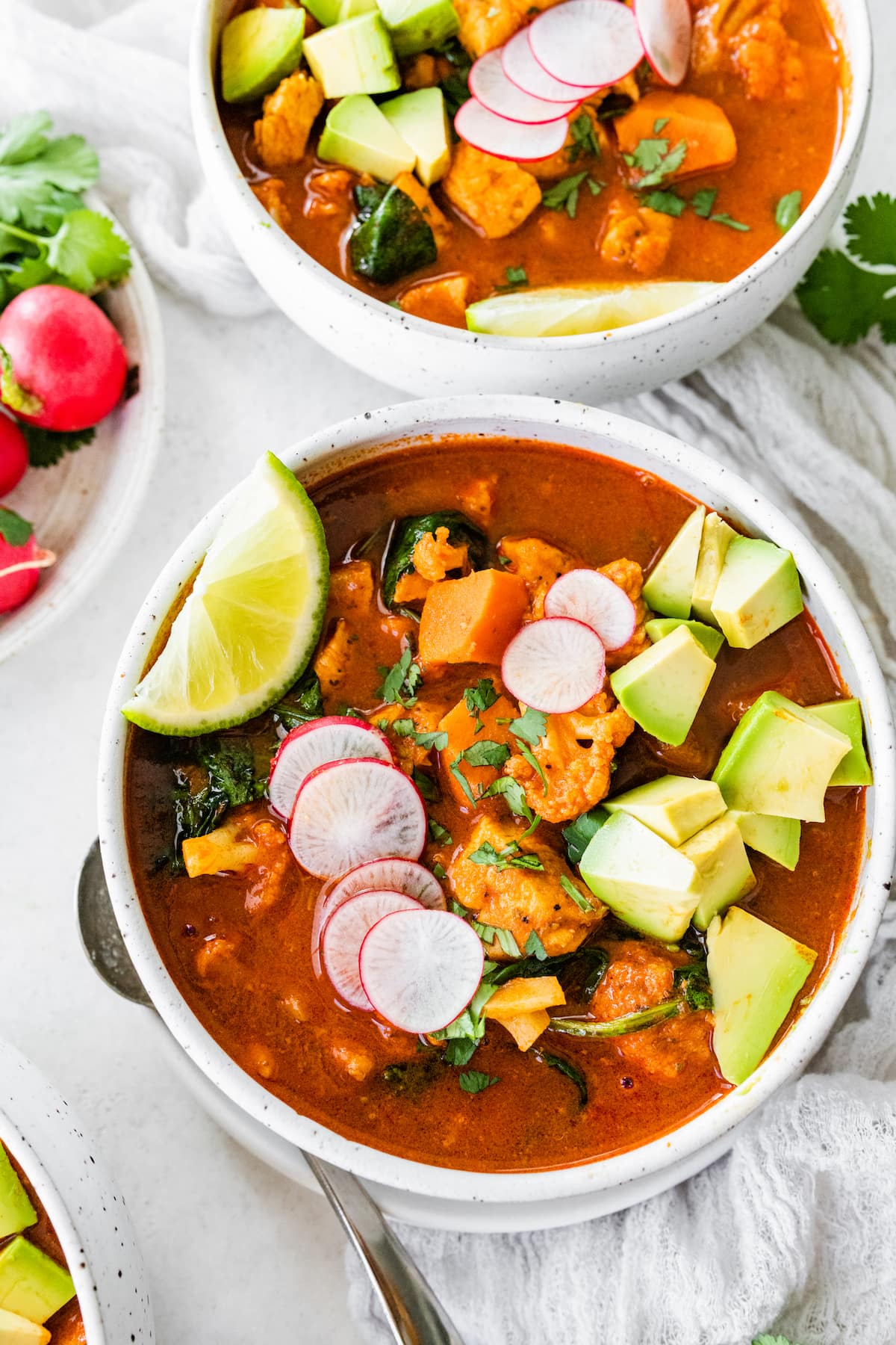 A bowl of Mexican sweet potato chicken soup topped with sliced radish, cilantro, avocado, and a lime wedge.