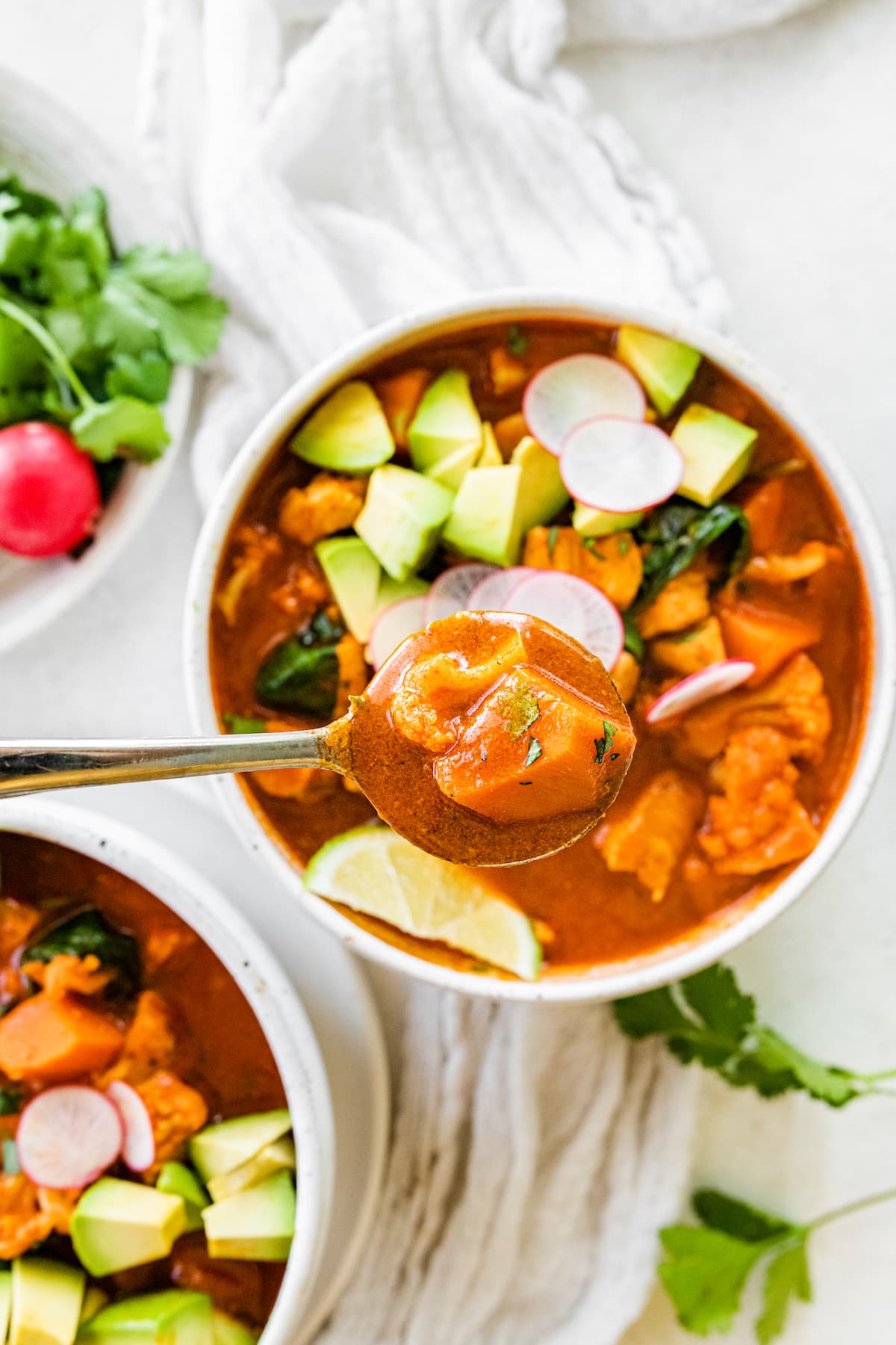 A bowl of Mexican sweet potato chicken soup with a spoon over the top of the bowl as if someone was going to take a bite.