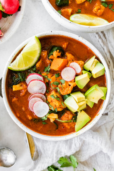 A bowl of Mexican sweet potato chicken soup topped with sliced radish, cilantro, avocado, and a lime wedge.