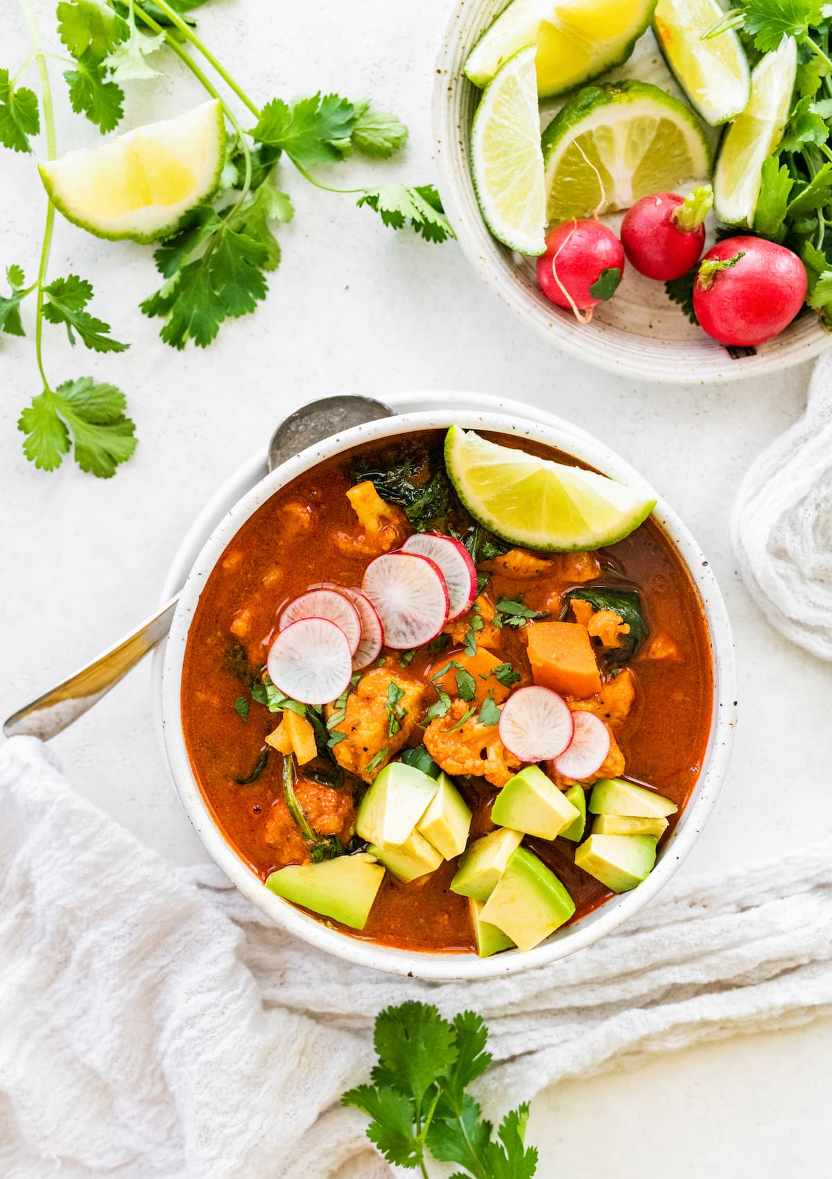 A bowl of Mexican sweet potato chicken soup topped with sliced radish, cilantro, avocado, and a lime wedge.