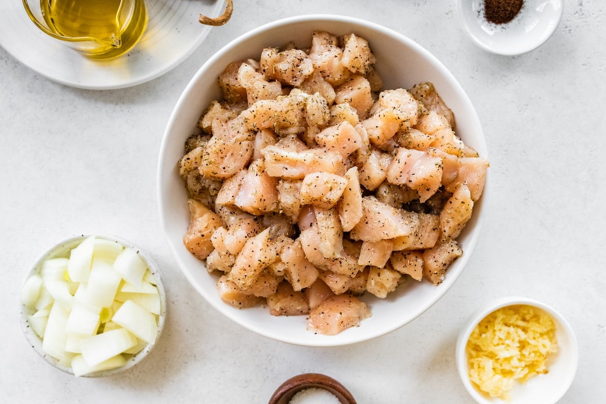 Raw chicken with herbs and spices in a white bowl.