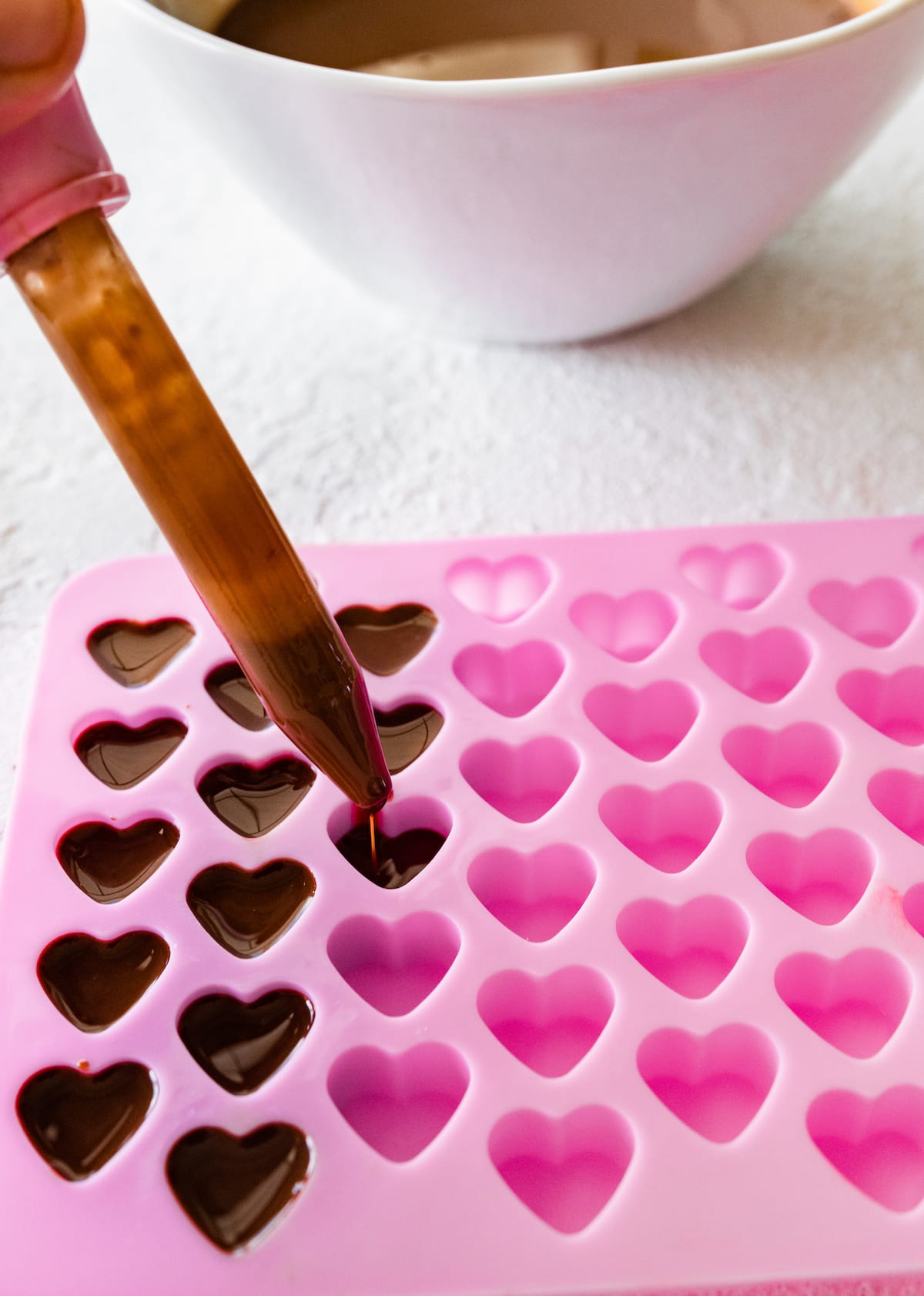 A small syringe pouring melted chocolate into a heart-shaped silicone mold.