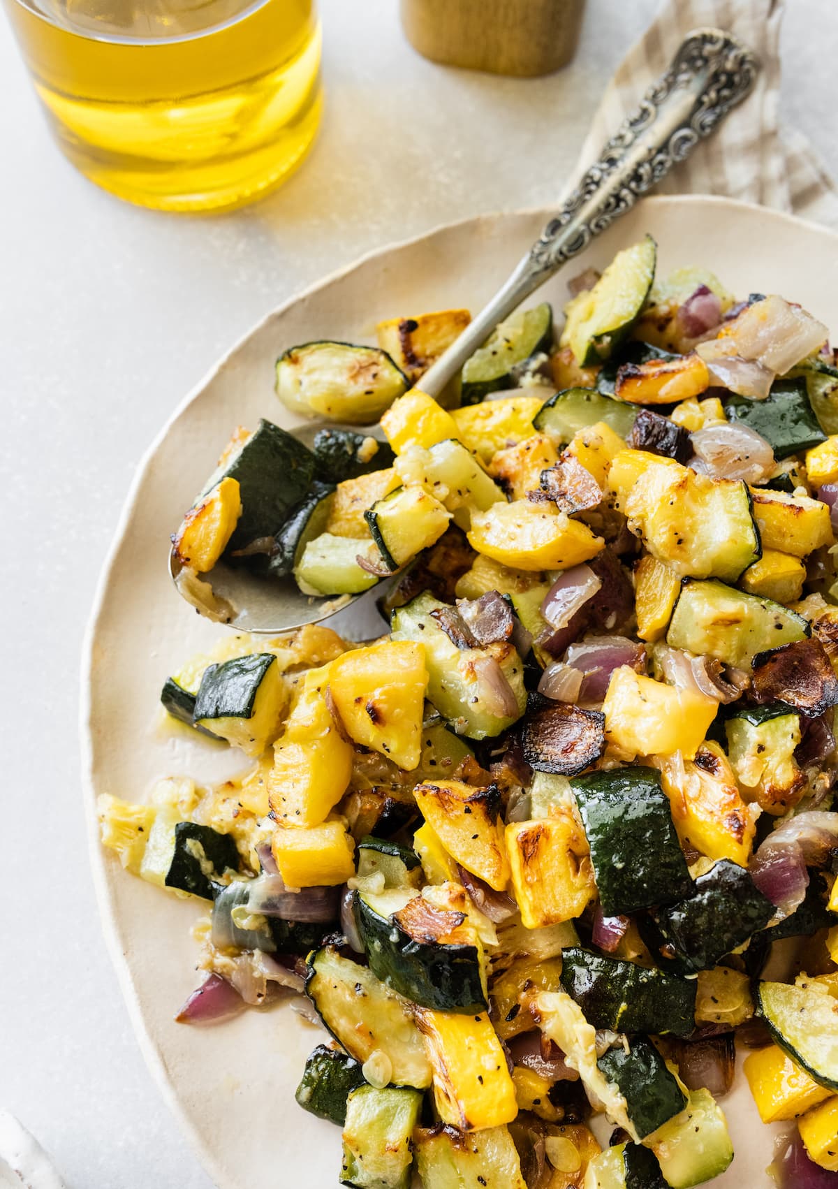 Roasted zucchini and squash on a white plate with a metal spoon.