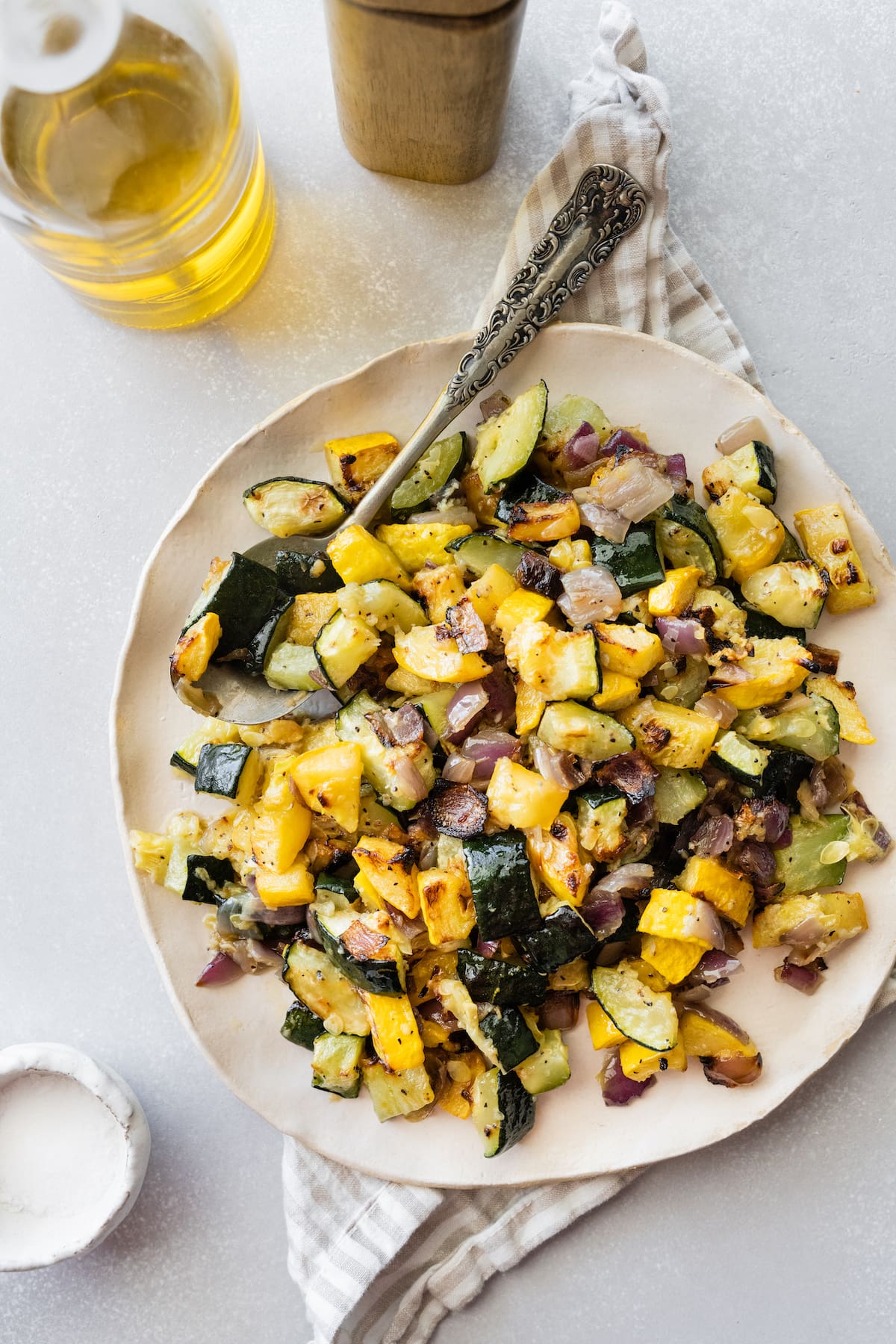 Roasted zucchini and squash on a white plate with a metal spoon.
