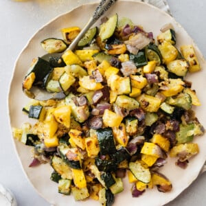 Roasted zucchini and squash on a white plate with a metal spoon.