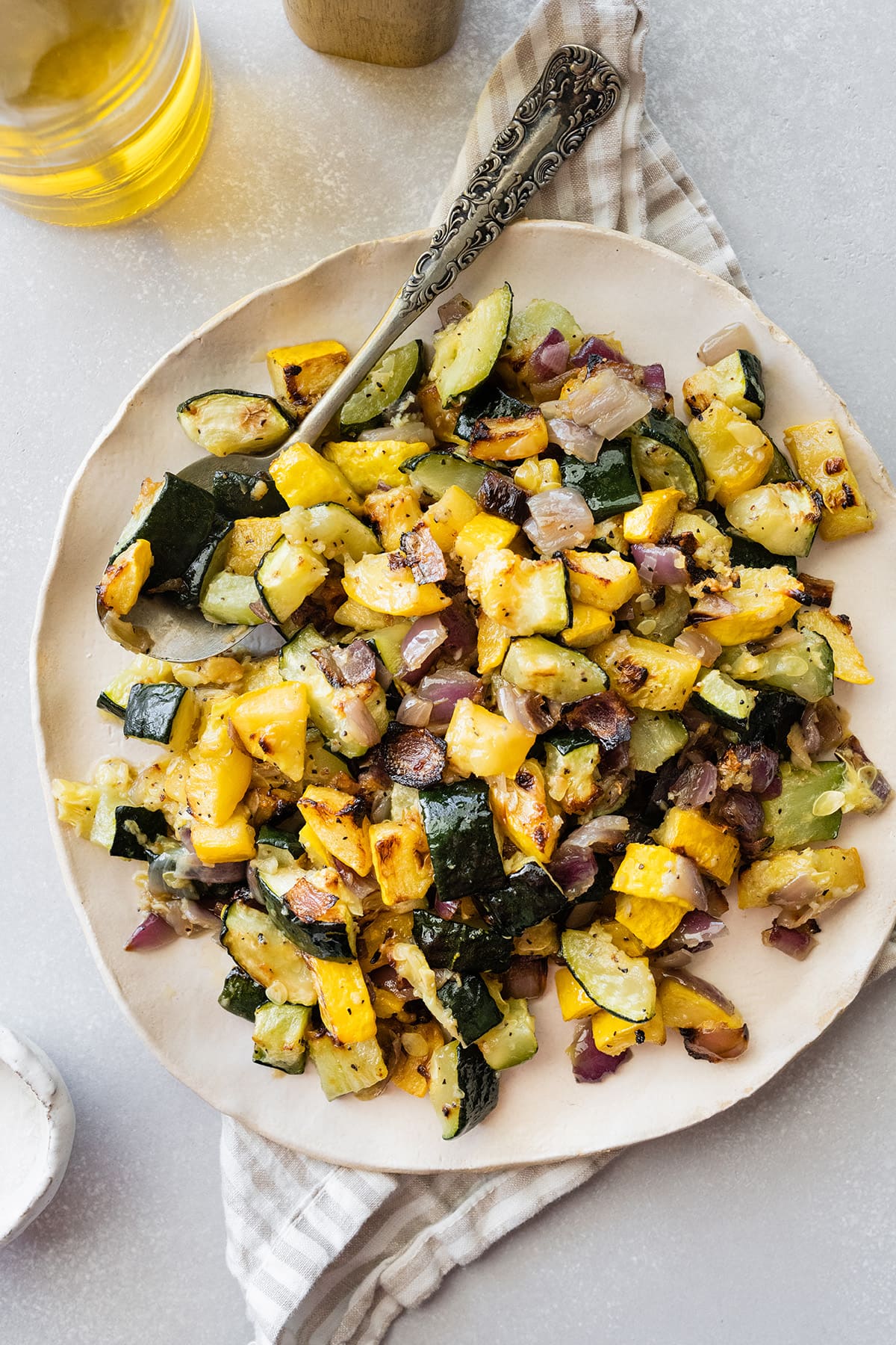 Roasted zucchini and squash on a white plate with a metal spoon.