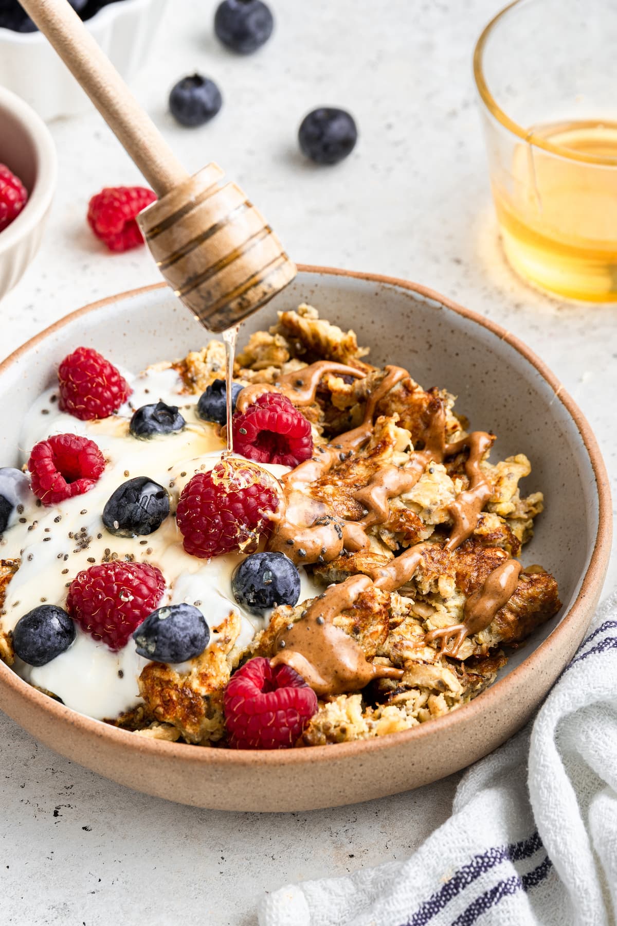 Honey is drizzled into a bowl of scrambled oats with a scoop of yogurt, chia seeds, fresh berries, and almond butter on top.