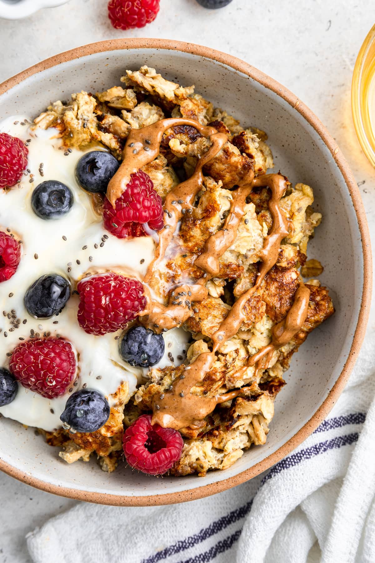 A bowl of scrambled oats with a scoop of yogurt, chia seeds, fresh berries, and a drizzle of almond butter on top.