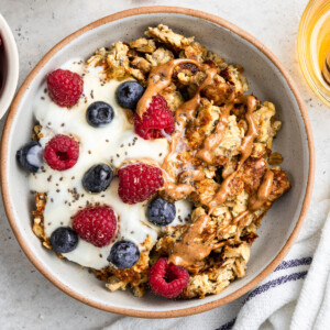 A bowl of scrambled oats with a scoop of yogurt, chia seeds, fresh berries, and a drizzle of almond butter on top.