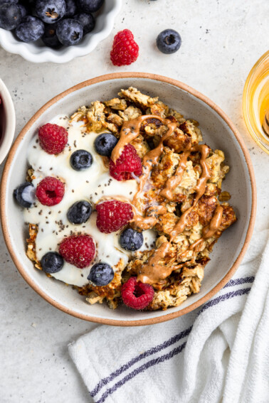 A bowl of scrambled oats with a scoop of yogurt, chia seeds, fresh berries, and a drizzle of almond butter on top.